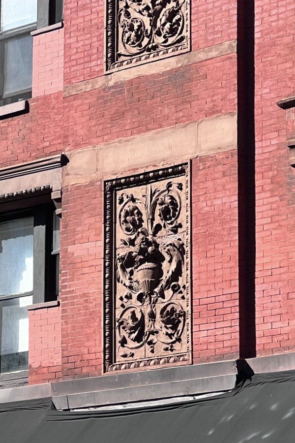 Red brick wall with a carved floral panel above a dark awning