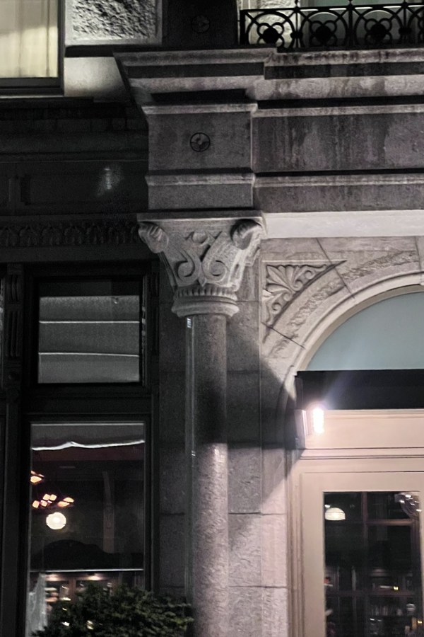 Dark stone building corner with a carved column capital and a lit doorway