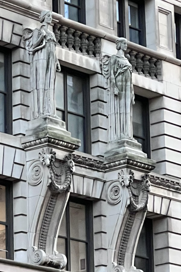 Stone facade with two sculpted figures on a balcony above scrolled brackets